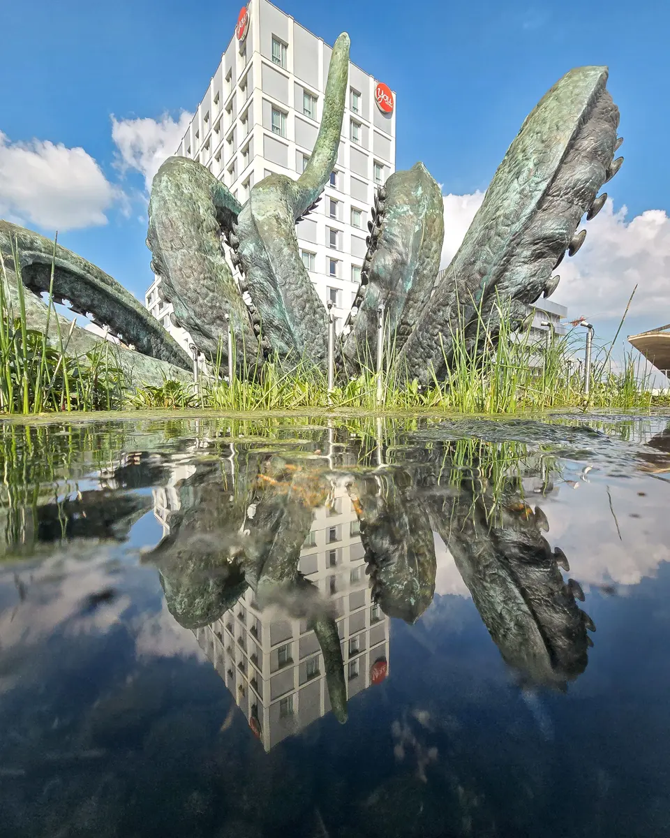 Une sculpture végétale et des immeubles se reflètent dans un bassin