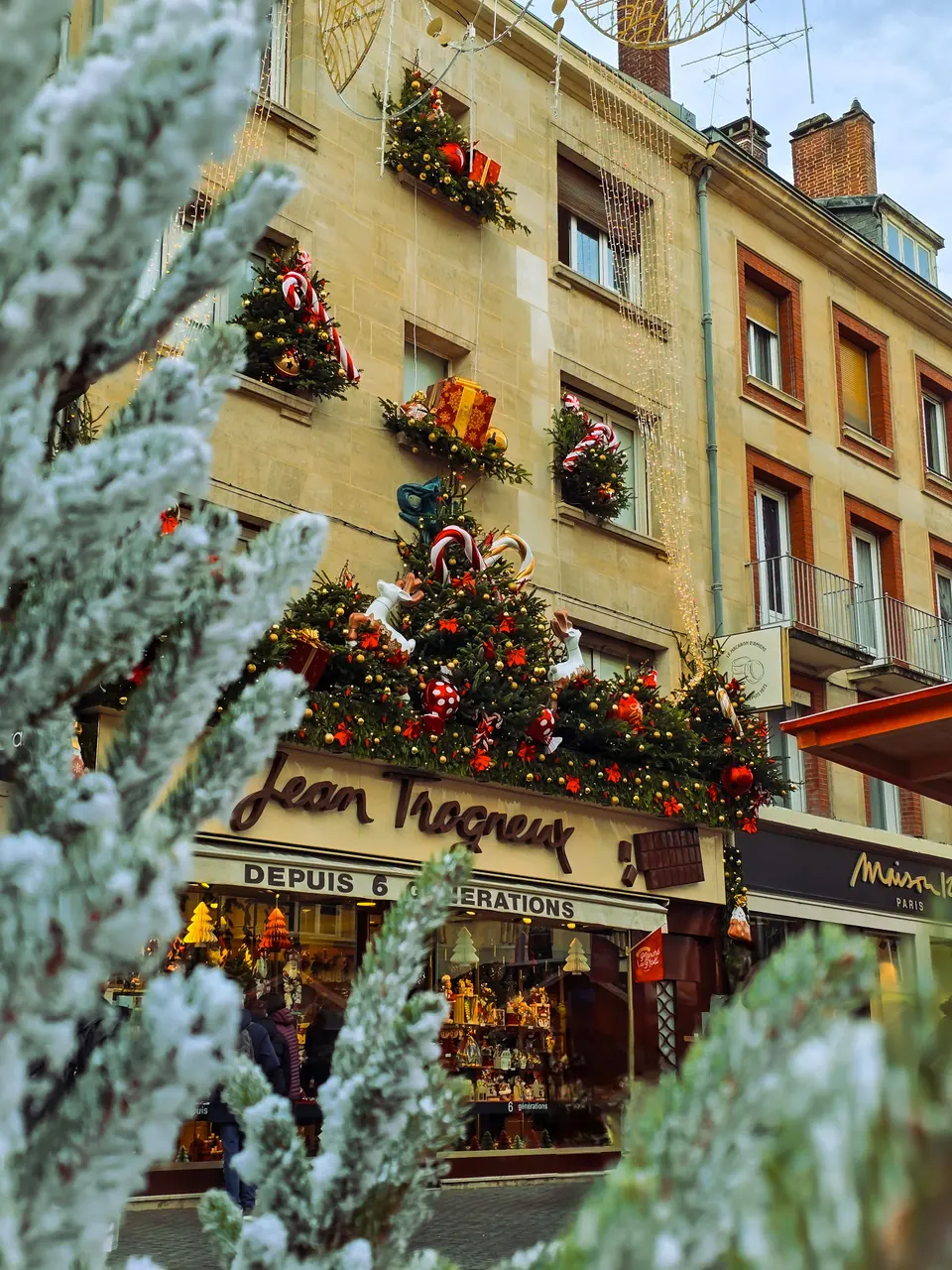 Une rue commerçante décorée pour Noël, vue à travers des branches de sapin