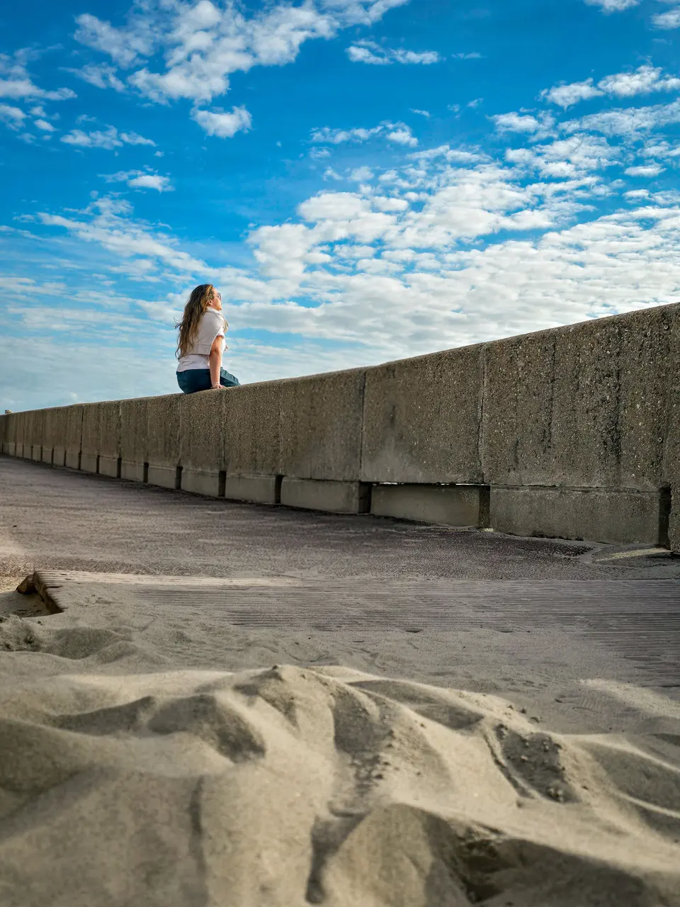 Une silhouette assise au sommet d'une digue, au-dessus des dunes et d'un grand ciel bleu
