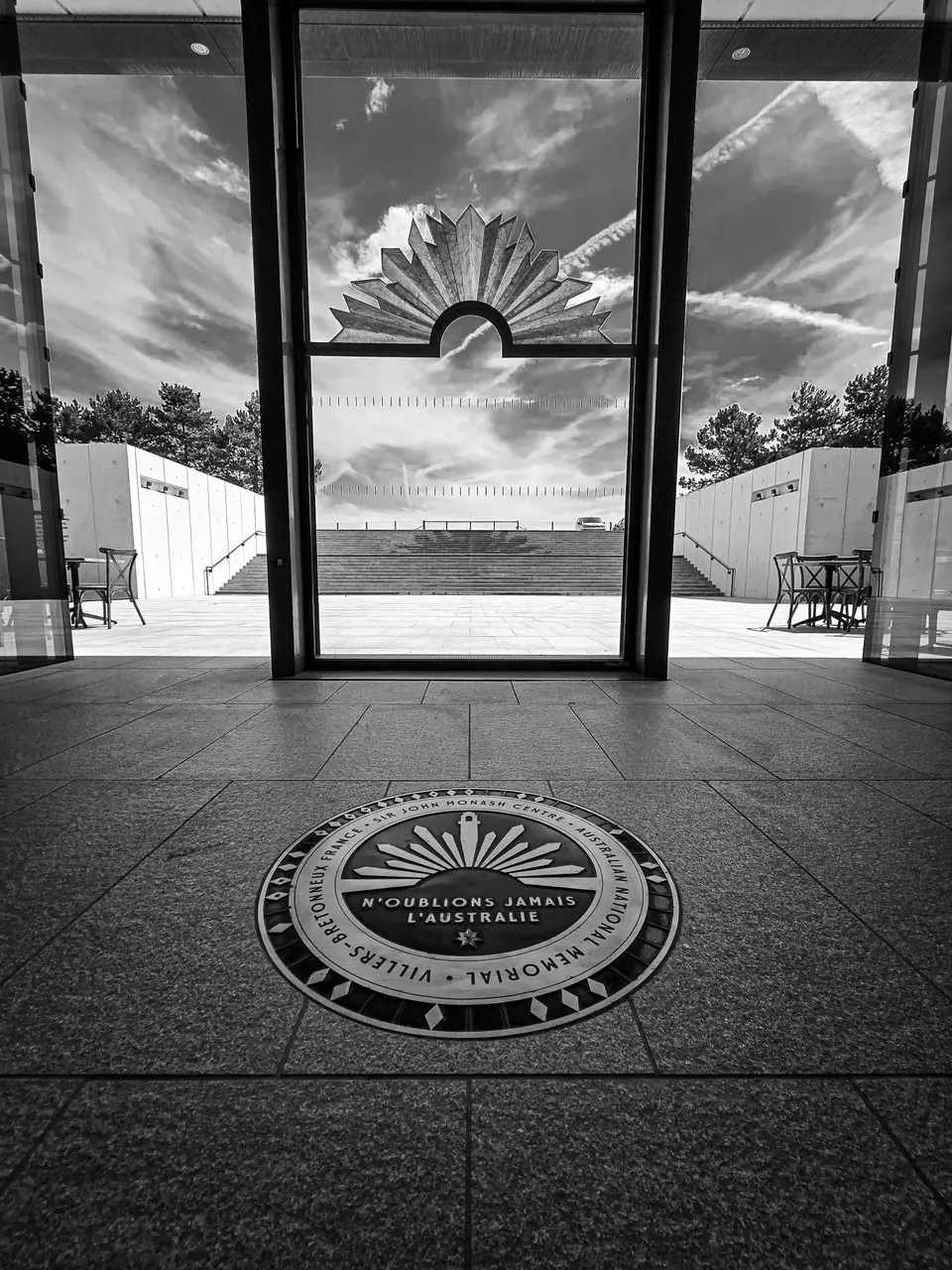Un grand hall vitré photographié en noir et blanc, un médaillon au sol