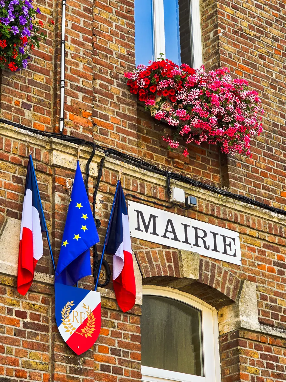 Façade de mairie en briques, drapeaux et jardinières fleuries