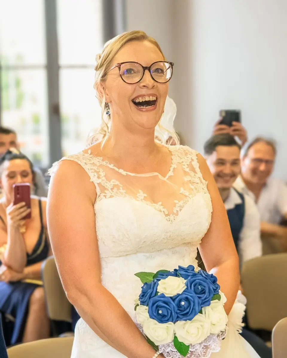La mariée éclate de rire, son bouquet bleu et blanc à la main
